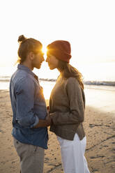 Romantic young couple standing face to face at beach during sunset - UUF21835