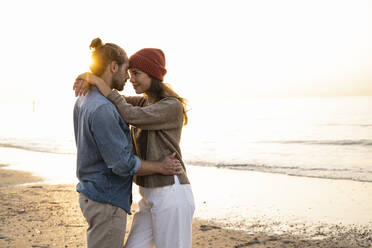 Romantic young couple standing face to face while looking at each other during sunset - UUF21837