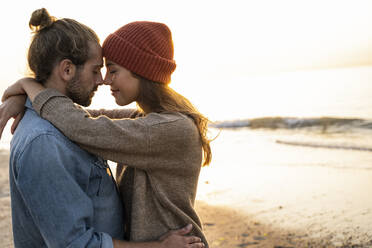 Romantisches junges Paar steht von Angesicht zu Angesicht mit geschlossenen Augen am Strand bei Sonnenuntergang - UUF21840