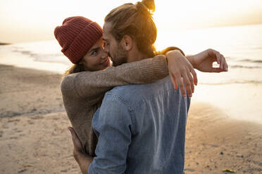 Smiling young woman embracing while looking at boyfriend during sunset - UUF21846