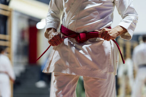 Aktiver älterer Mann, der den Gürtel festzieht, während er im Unterricht Karate übt - OCMF01791
