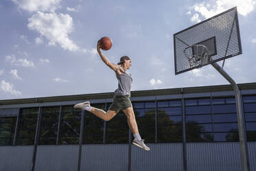Young male athlete practicing dunking ball in basketball hoop on sunny day - STSF02623