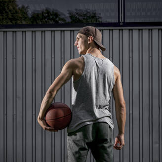 Junger Mann hält Ball und schaut weg auf Basketballplatz - STSF02625