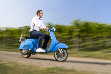 Handsome young man riding motor scooter on road by vineyard - STSF02627