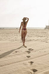 Young woman wearing bikini with hand in hair walking at beach - AJOF00326