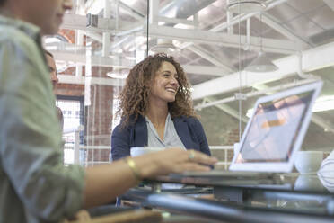 Smiling woman sitting with team while working at office - AJOF00329