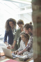 Smiling team of employees working on laptop while standing in office - AJOF00341