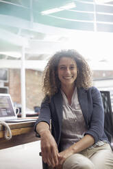 Smiling young woman sitting on chair at office - AJOF00343