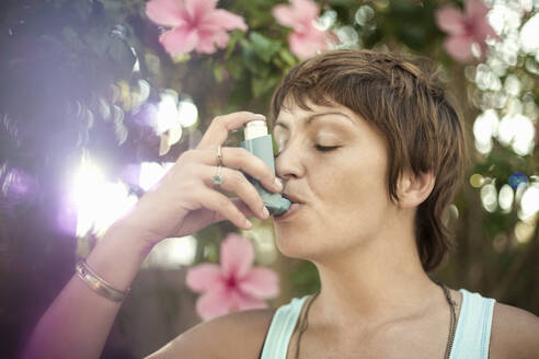 Young woman breathing through asthma inhaler - AJOF00344