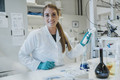 Smiling woman pipette while standing at laboratory - MFF06448