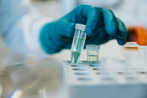 Woman wearing protective glove holding test tube while standing at laboratory  stock photo