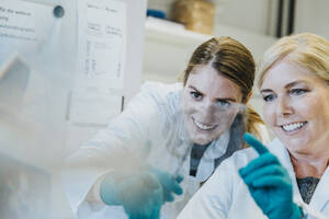 Lächelnde Wissenschaftlerin und Assistentin diskutieren bei der Untersuchung eines Objektträgers mit menschlichem Gehirn im Labor - MFF06459