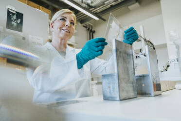 Smiling scientist removing microscope slide while standing at laboratory - MFF06461