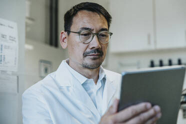 Wissenschaftler mit Brille, der im Labor stehend an einem digitalen Tablet arbeitet - MFF06479