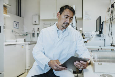 Männlicher Wissenschaftler, der ein digitales Tablet benutzt, während er im Labor sitzt - MFF06483