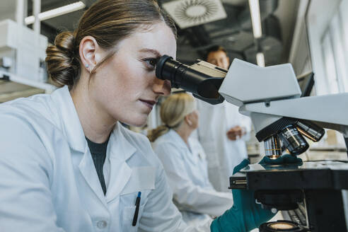 Assistant analyzing human brain microscope slide while sitting with scientist in background at laboratory - MFF06491