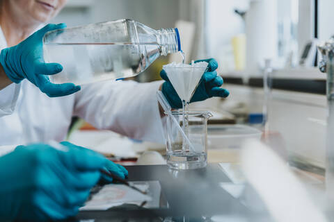 Scientist pouring filtering liquid while standing at laboratory stock photo