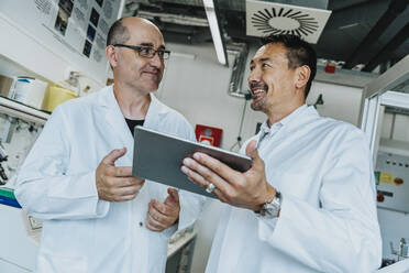Lächelnde Wissenschaftler, die ein digitales Tablet benutzen, während sie im Labor stehen - MFF06533