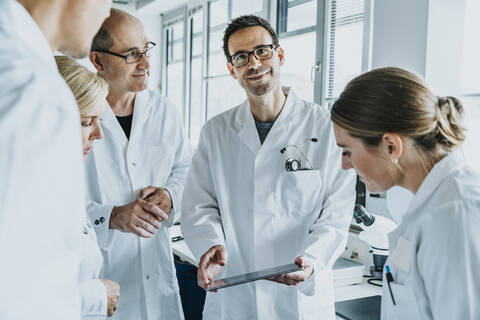 Smiling scientist holding digital tablet while standing by coworkers at laboratory stock photo