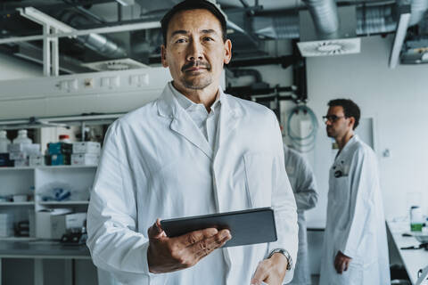 Scientist using digital tablet while standing with coworker in background at laboratory stock photo