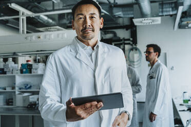 Wissenschaftler, der ein digitales Tablet benutzt, während er mit einem Mitarbeiter im Hintergrund im Labor steht - MFF06556