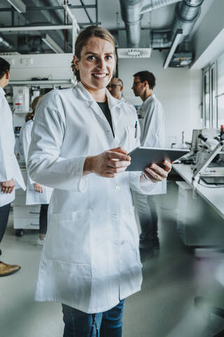 Smiling female using digital tablet while standing with coworker in background at laboratory stock photo