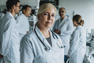 Lächelnde Wissenschaftlerin, die wegschaut, während sie mit einem Mitarbeiter im Hintergrund im Labor steht - MFF06571