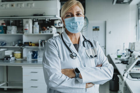 Confident scientist wearing face mask standing with arms crossed at laboratory stock photo