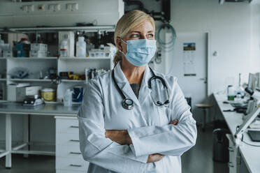 Female scientist wearing face mask standing with arms crossed at laboratory - MFF06574