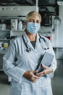 Scientist with face mask and digital tablet standing at laboratory - MFF06578