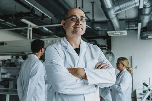 Selbstbewusster Wissenschaftler mit einem Mitarbeiter im Hintergrund im Labor stehend - MFF06581