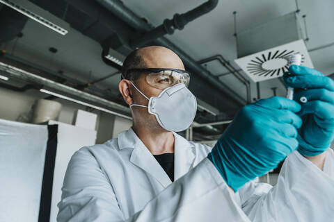 Scientist wearing protective face mask and eyeglasses holding vaccine while standing at laboratory stock photo