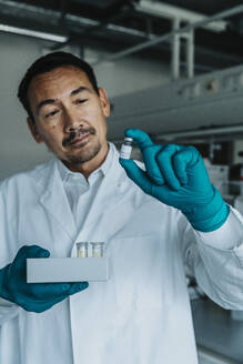 Wissenschaftler, der eine Impfstoffflasche und ein Reagenzglasfach hält, während er im Labor steht - MFF06594