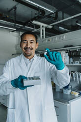 Smiling scientist holding vaccine while standing at laboratory - MFF06595