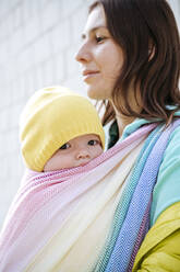 Mutter hält ihr in eine Decke eingewickeltes Baby und schaut an einem sonnigen Tag weg - EYAF01370