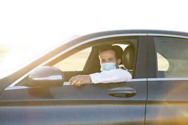Man wearing protective mask while sitting in car during coronavirus - CJMF00336
