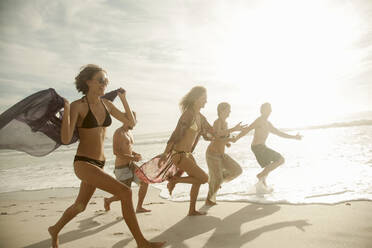 Group of friends running at beach on sunny day - AJOF00353