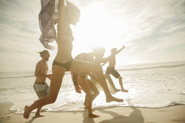 Cheerful friends jumping at beach on sunny day - AJOF00354