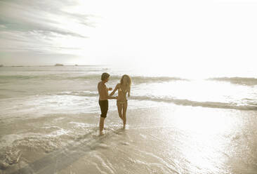 Couple standing in water at beach on sunny day - AJOF00358