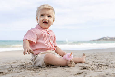 Smiling baby boy sitting on the beach - DLTSF01415