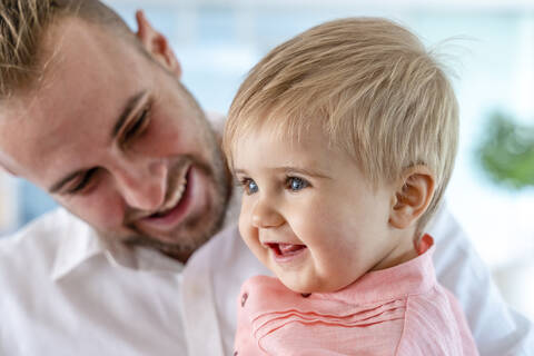 Father looking at smiling baby while standing indoors stock photo