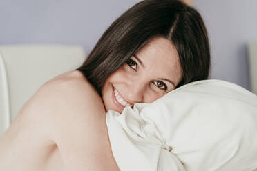 Smiling beautiful woman hugging blanket in bedroom at home - EBBF01014