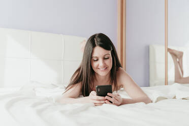 Lächelnde schöne Frau Text-Messaging, während auf dem Bett zu Hause liegen - EBBF01016