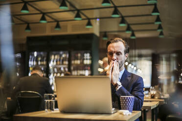 Besorgter Geschäftsmann schaut im Restaurant auf seinen Laptop - MASF20056