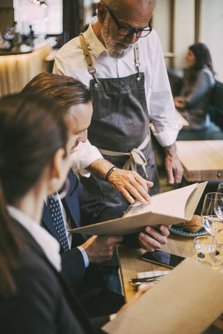 Waiter standing by table while business professionals sitting in restaurant stock photo