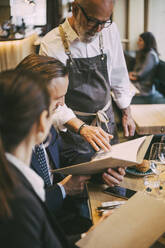 Kellner steht am Tisch, während Geschäftsleute im Restaurant sitzen - MASF20077