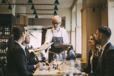 Kellner gibt Geschäftsleuten im Restaurant die Speisekarte - MASF20078