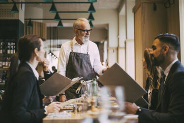 Kellner im Gespräch mit Geschäftsleuten, während er am Tisch im Restaurant steht - MASF20082