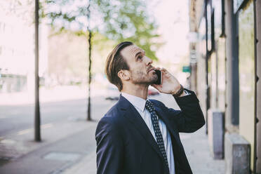 Side view of businessman talking on phone in city - MASF20103