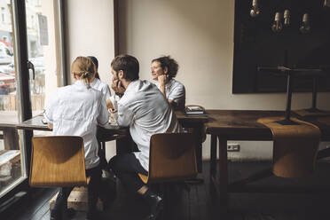 Männlicher Chefkoch diskutiert mit weiblichen Mitarbeitern am Tisch im Restaurant - MASF20117